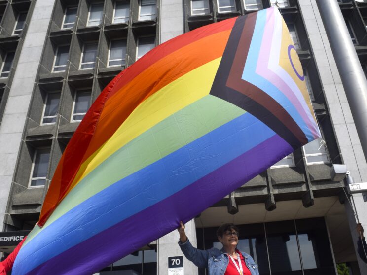 Participants marching in Pride Week parade holding a rainbow banner